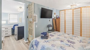 A bedroom with a bed, a desk with a chair, a television, a wardrobe, and a ceiling light.