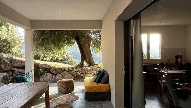 Um espaço de estar moderno com uma mesa de madeira, banquetes, um sofá e vista para uma paisagem natural.
