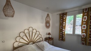 Um quarto com cama, mesa de cabeceira, luminária e janela com cortinas.