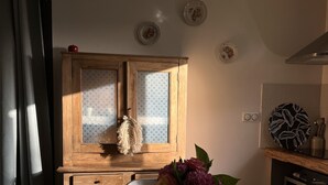 Uma mesa de jantar de madeira com cadeiras, um vaso com flores e um armário de madeira com portas de vidro jateado.