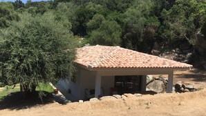 Um pequeno edifício com telhado em tijolos, rodeado por árvores e pedras.