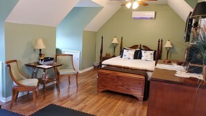 Ein Schlafzimmer mit schrägem Dach, einem Bett mit Holz Kopfteil, einem Schreibtisch mit Stuhl und einem Nachttisch mit Lampen.