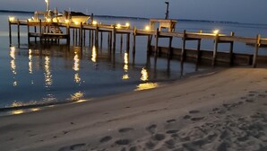 Eine hölzerne Pier erstreckt sich in ruhiges Wasser bei Dämmerung, entlang ihrer Länge sind Lichter angebracht.