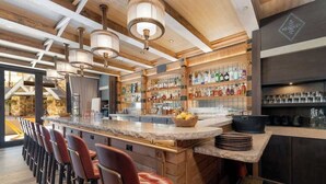 A modern bar area with a long counter, multiple stools, and a variety of bottles and glasses. - 5 Star Hotel - Exclusive Private Residence (Mountain Village)