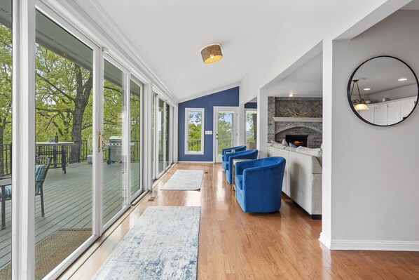 Un vaste espace de vie doté d’une grande porte-fenêtre coulissante donnant sur une terrasse extérieure, d’une cheminée et d’un coin salon avec des fauteuils bleus.