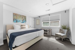 Une chambre à coucher avec un lit, un bureau, une chaise, une fenêtre et un tableau accroché au mur.