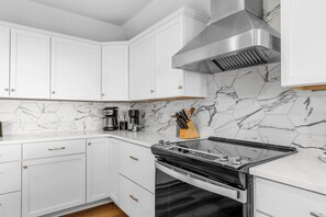 Une cuisine moderne avec des armoires blanches, une hotte en acier inoxydable, une cuisinière noire et un dosseret en marbre hexagonal.