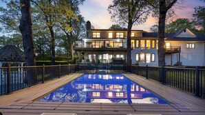 A swimming pool with a wooden deck and metal railings, surrounded by trees and a two-story building with balconies. - Ultimate Lakeview w/ Private Outdoor Pool, Hot Tub, Yard, Karaoke, Billiards, Arcade & Free Tickets (Branson)