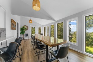 Un espace de restauration moderne avec une longue table, des chaises noires et de grandes fenêtres donnant sur l’extérieur.