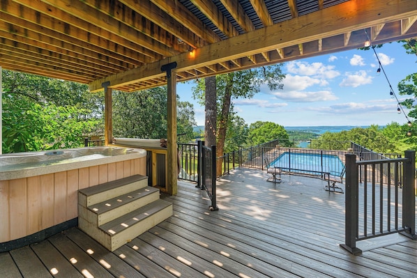 A wooden deck with a hot tub, pool, and outdoor seating area, overlooking a scenic landscape.