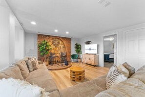 A modern living room with a brick accent wall, a wooden coffee table, and a television. - Ultimate Lakeview w/ Private Outdoor Pool, Hot Tub, Yard, Karaoke, Billiards, Arcade & Free Tickets (Branson)