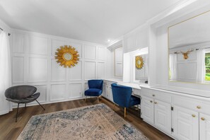 A room with white paneled walls, a blue chair, a vanity with a mirror, and a decorative sunburst mirror. - Ultimate Lakeview w/ Private Outdoor Pool, Hot Tub, Yard, Karaoke, Billiards, Arcade & Free Tickets (Branson)