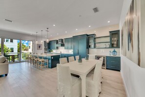 A modern kitchen with teal cabinets, a white dining area, and a large window overlooking a garden.