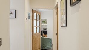 Un couloir avec une porte en bois, un lit vert et un mur blanc orné d’un tableau encadré.