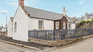 Une maison à deux étages, avec une façade blanche, un toit gris et une clôture en bois.