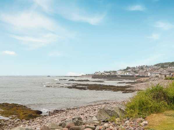 A coastal town with a rocky shoreline, a clear sky, and buildings in the background.