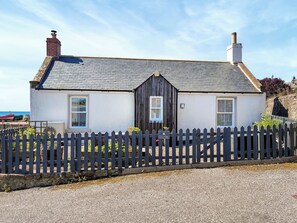 Une petite maison de campagne à deux étages, avec une clôture en piquets, une cheminée et un petit jardin.