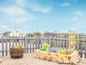 Ein Garten mit erhöhten Beeten, einem hölzernen Spalier, einem Holzbottich und einem Holzzaun.