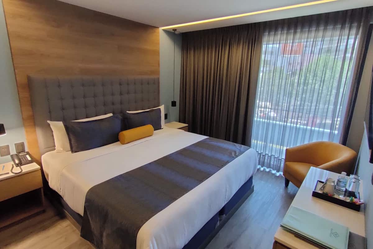 A modern hotel room with a large bed, a desk with a telephone, and a chair.