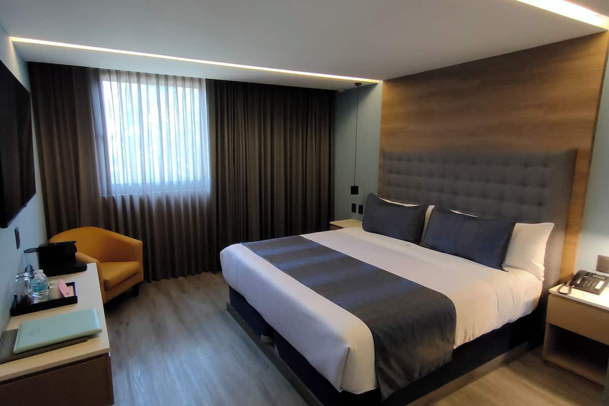 A modern hotel room with a large bed, a desk with a laptop, a chair, and a TV mounted on the wall.