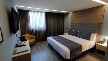 Ein modernes Hotelzimmer mit einem großen Bett, einem Schreibtisch mit einem Laptop, einem Stuhl und einem an der Wand befestigten Fernseher.