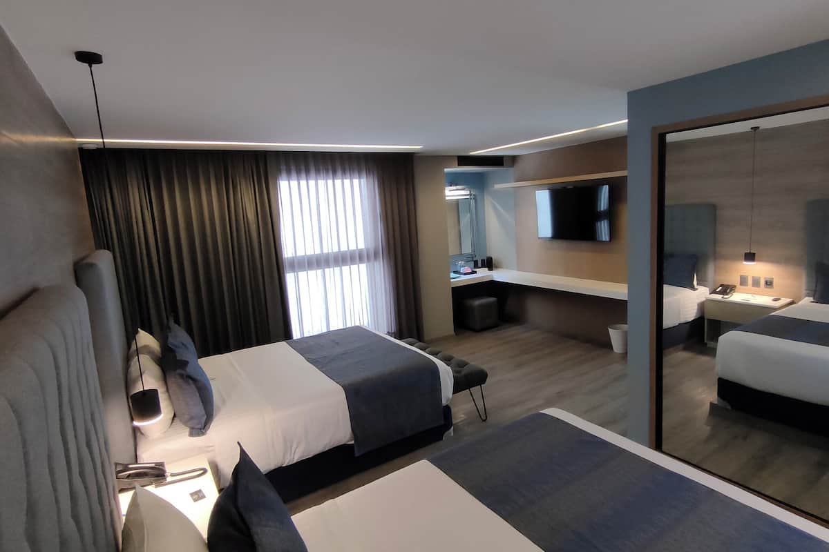 A modern hotel room with a large bed, a desk, a mirror, and a TV.