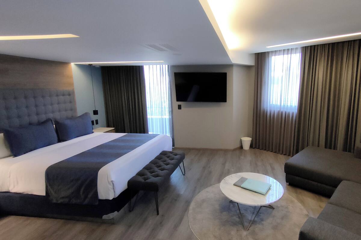 A modern hotel room with a large bed, a sofa, a coffee table, and a TV.