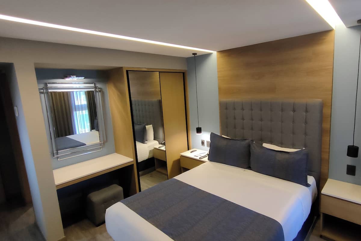 A modern hotel room with a large bed, a desk, a chair, and a wardrobe.