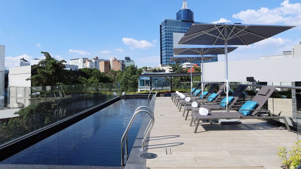 A rooftop pool area with lounge chairs and umbrellas, a clear view of the city skyline, and a modern building in the background. - Alia Inn Boutique WTC (Mexico City)