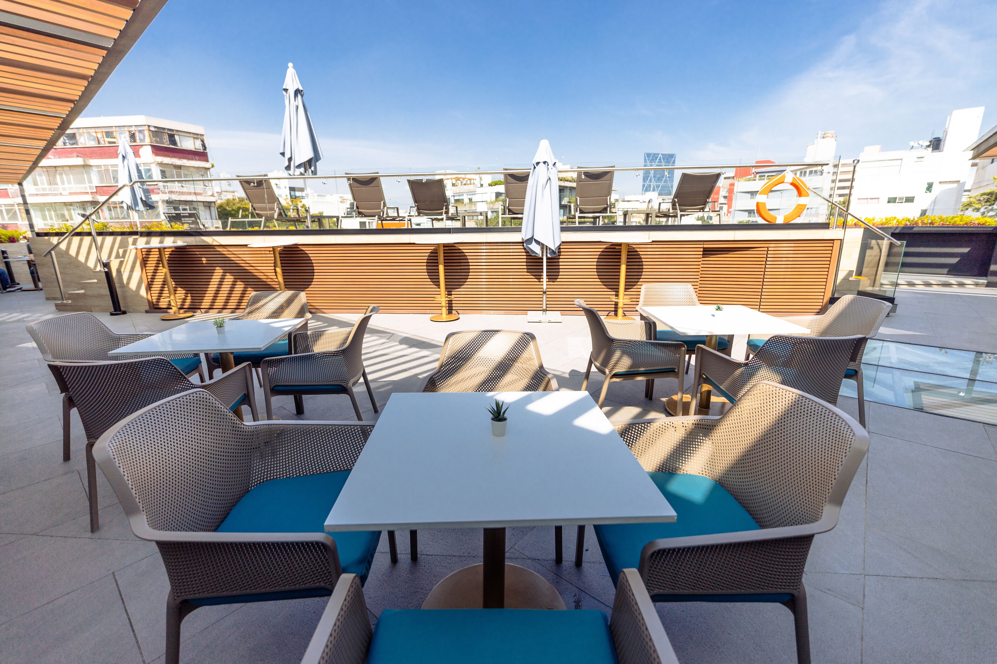 An outdoor seating area with tables and chairs, a small potted plant, and a view of buildings in the background.