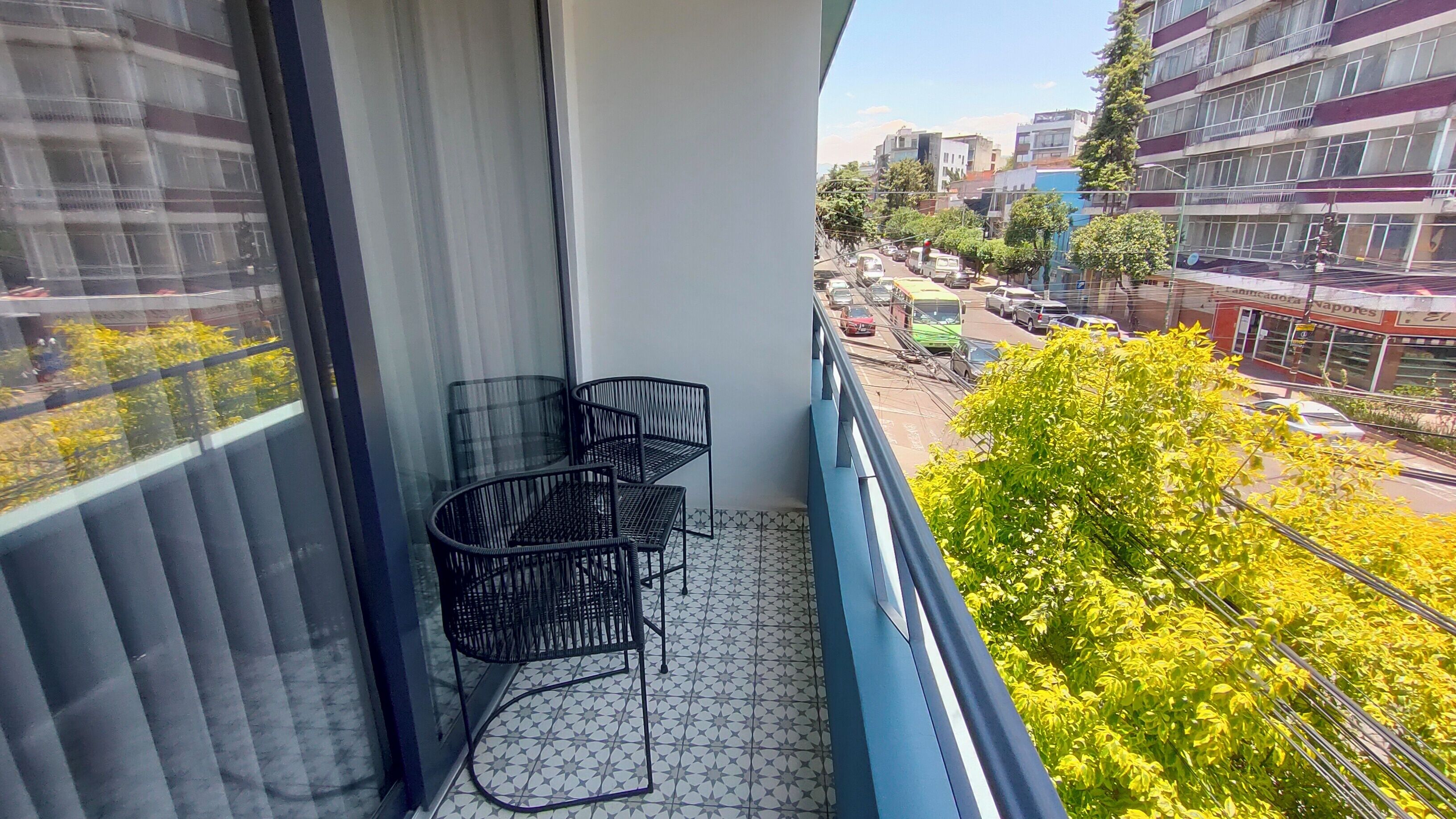 A balcony with a view of a city street, a tiled floor, and two black metal chairs.