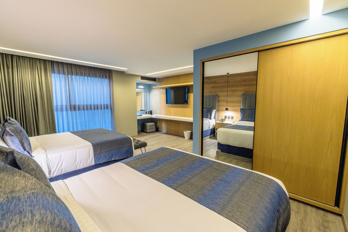 A hotel room with two beds, a desk, a mirror, and a wardrobe.