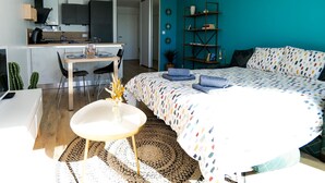 A modern bedroom with a bed, bedside tables, a desk, and a chair. There is a kitchen area in the background. - Renovated studio facing the main beach in Les Sables d'Olonne (Les Sables-d´Olonne)