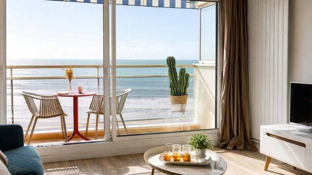 A room with a large window overlooking the sea, a small table with drinks, a cactus plant, and a TV on a stand. - Renovated studio facing the main beach in Les Sables d'Olonne (Les Sables-d´Olonne)
