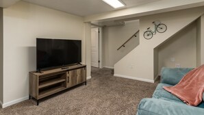En stue med et fjernsyn på et træstel, en turkis sofa og en trappe med en cykelpynt.