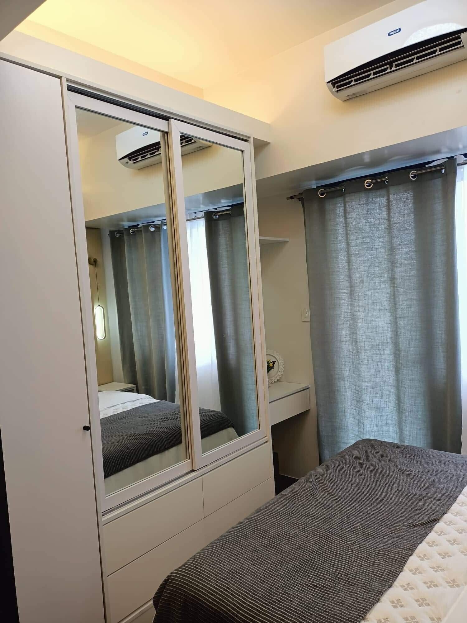 Ein Hotelzimmer mit großem Kleiderschrank, einem Bett, einem kleinen Nachttisch und einer Klimaanlage.