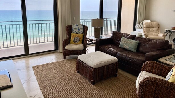 A spacious living room with a large view of the ocean, a ceiling fan, and a comfortable seating area with a sofa and armchairs. - Expansive Ocean front views—direct beach access! (New Smyrna Beach)