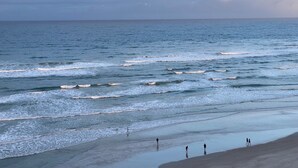 A beach with waves and a few people walking along the shore. - Expansive Ocean front views—direct beach access! (New Smyrna Beach)