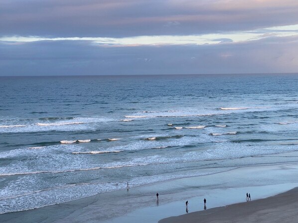 A beach with waves and a few people walking along the shore.