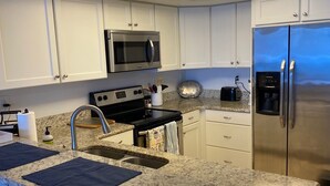 A modern kitchen with white cabinets, a stainless steel refrigerator, a microwave, and a built-in oven. - Expansive Ocean front views—direct beach access! (New Smyrna Beach)