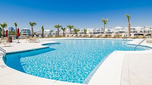 A swimming pool with a clear blue water, surrounded by lounge chairs and palm trees.