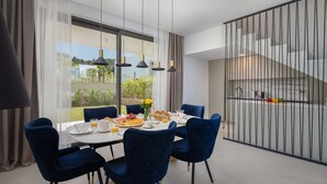 Un comedor moderno con una mesa grande, sillas azules y vistas a un jardín a través de grandes ventanales.