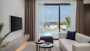 Ein modernes Wohnzimmer mit großem Fenster, einem Flachbildfernseher, einer Couch, einem Couchtisch und Blick auf Pool und Meer.