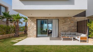 Ein modernes Haus mit Natursteinfassade, einer Glastür, die auf eine Terrasse führt, und Blick aufs Meer.