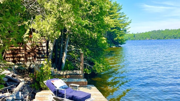 A wooden dock extending into a lake, with a lounge chair and a small table.