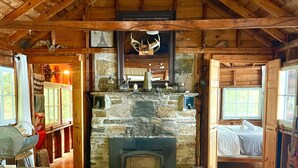 A rustic cabin interior with a stone fireplace, wooden beams, a sofa, and a bed.
