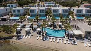 Un resort moderno con varias edificaciones blancas, una piscina central y palmeras.