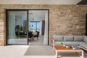 A modern living room with a stone wall, a sliding glass door leading to a balcony, a grey sofa, and a wooden coffee table.