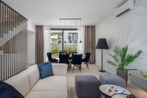 A modern living room with a sofa, ottoman, and a dining area with chairs and a table.