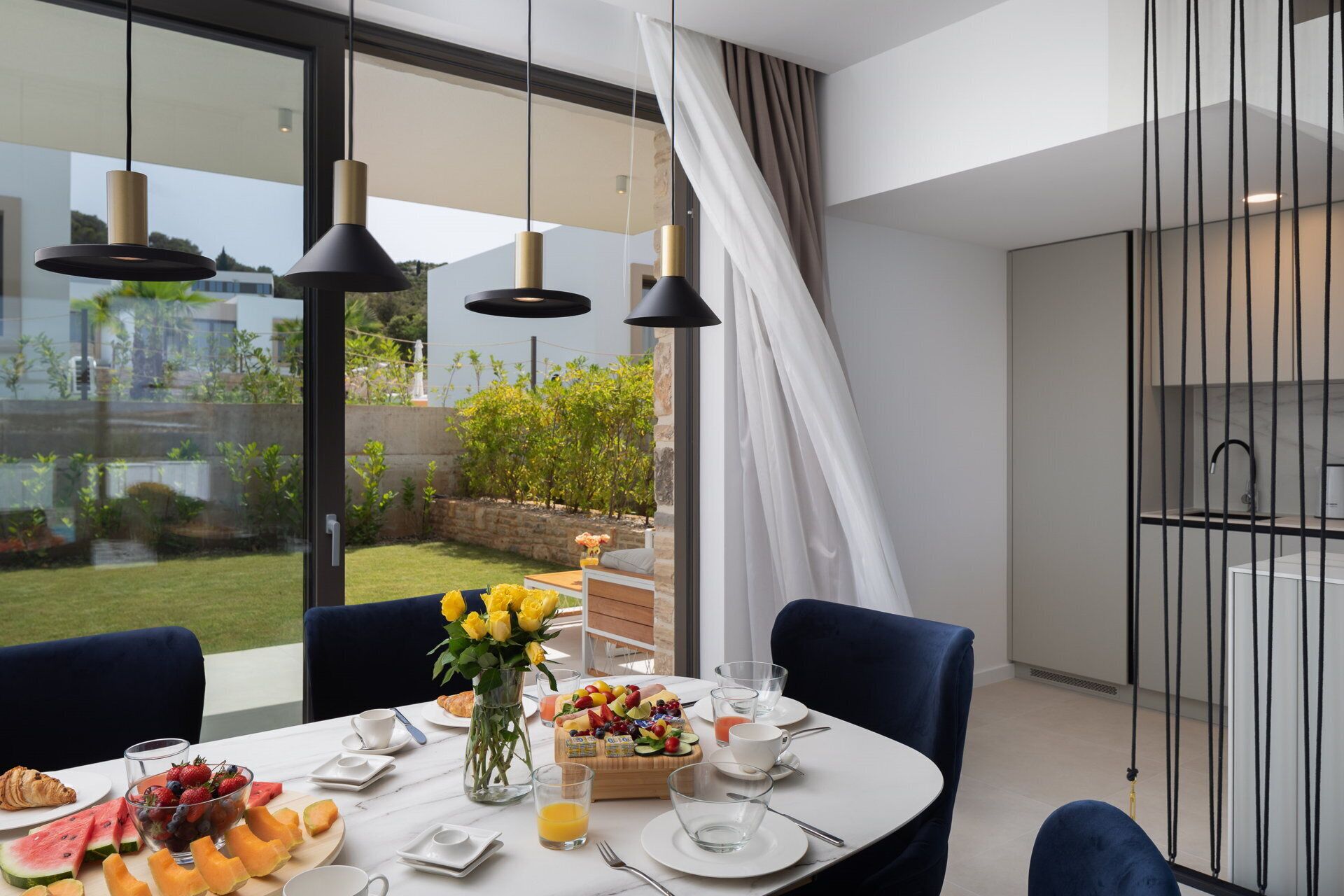 Un comedor moderno con una mesa dispuesta para el desayuno, con frutas, pasteles y bebidas.